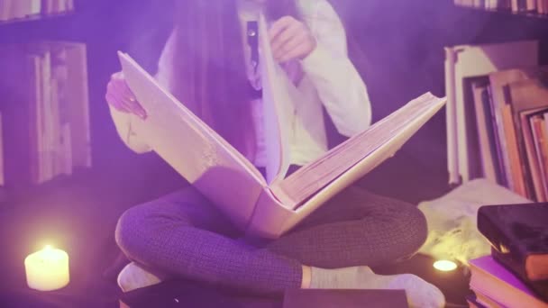 Ένα κορίτσι ανοίγει ένα παραμυθένιο βιβλίο στη βιβλιοθήκη, έγχρωμος καπνός στροβιλίζεται γύρω, κεριά ανάβουν κοντά - Πλάνα, βίντεο