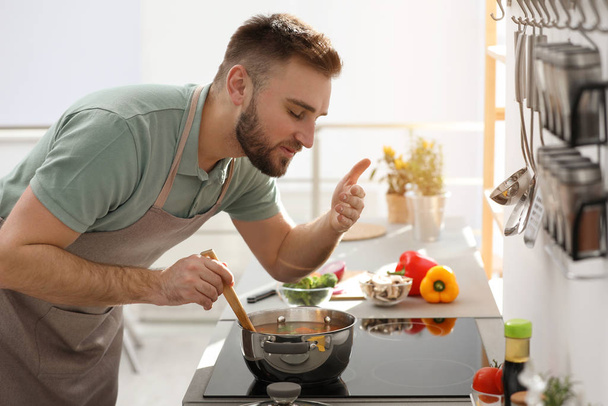 Young man cooking delicious soup in kitchen - Foto, Imagem