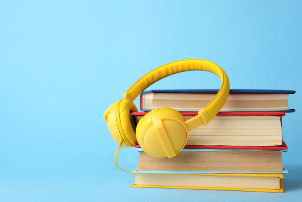 Books and modern headphones on light blue background. Space for text - Foto, Imagem