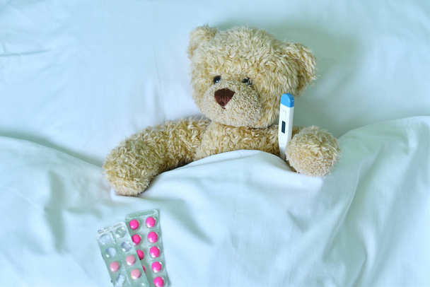 Urso de pelúcia com um termômetro eletrônico na cama
 - Foto, Imagem