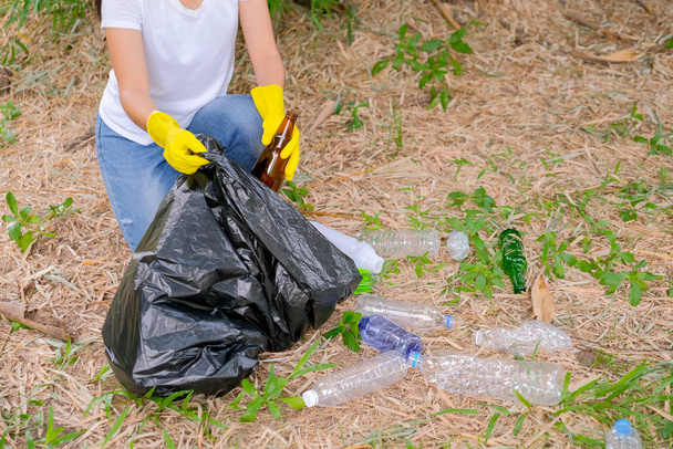 Ręce białej koszuli kobieta zbierać śmieci z traw i gleby do czarnej torby w ogrodzie z koncepcją uratować środowisko. - Zdjęcie, obraz