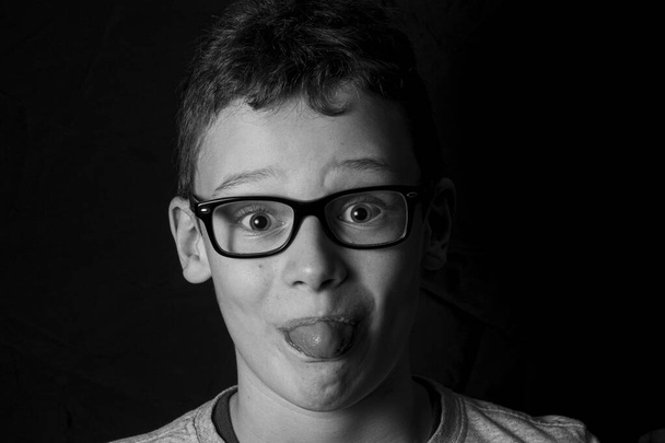 Junge mit Brille streckt die Zunge heraus und blickt schwarz-weiß in die Kamera - Foto, Bild