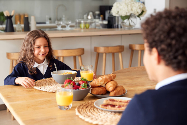 Children Wearing Uniform In Kitchen Eating Breakfast Before Going To School - Foto, Imagen