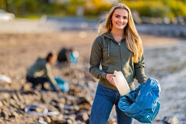 Freiwillige halten Flasche und Müllsack am Strand - Foto, Bild