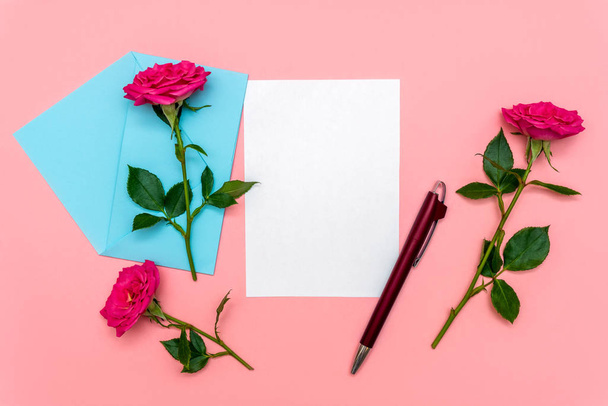 Walentynki lub inny pomysł na wakacje. Zdjęcie listu i papierowej koperty z kwiatami róż leżącymi na miękkim różowym tle. Makieta na zaproszenia ślubne lub list miłosny - Zdjęcie, obraz