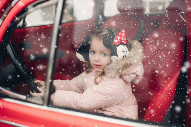Krásná holčička v ušních manžetách sedí v červeném autě. - Fotografie, Obrázek