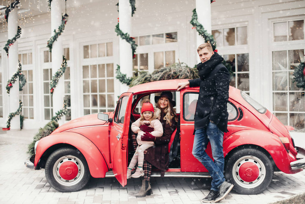Stijlvolle familie in rode auto buiten met Kerstmis. - Foto, afbeelding