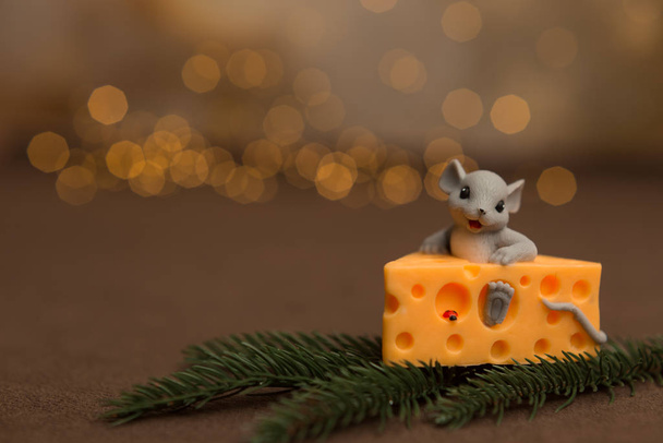 Eine Spielzeugmaus sitzt in Käse auf einem hölzernen Sternenhintergrund mit einem Zweig aus Fichten und Weihnachtskugeln. Symbol für 2020. - Foto, Bild