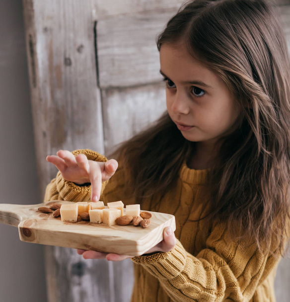 Κοριτσάκι ποζάρει με τυρί σε ξύλινη σανίδα - Φωτογραφία, εικόνα