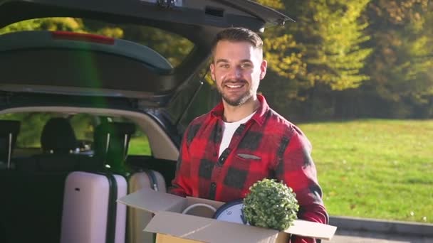 Joyeux jeune homme attrayant dans des vêtements modish tenant boîte de carton, debout près de l'auto et posant sur la caméra avec un beau sourire
 - Séquence, vidéo
