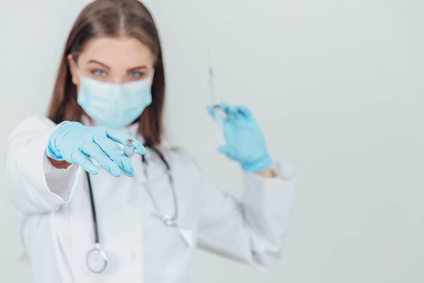 Blurred evil female doctor in medical mask holding syringes, pointing one of them at the camera. - Fotografie, Obrázek