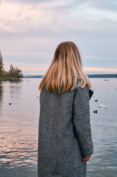 Beautiful blond hair woman enjoy panorama by the Bodensee lake. Landscape in Switzerland. Happy girl in travel. Amazing scenic outdoors view. Dramatic sky. Swans on water. Adventure lifestyle, freedom - Fotografie, Obrázek