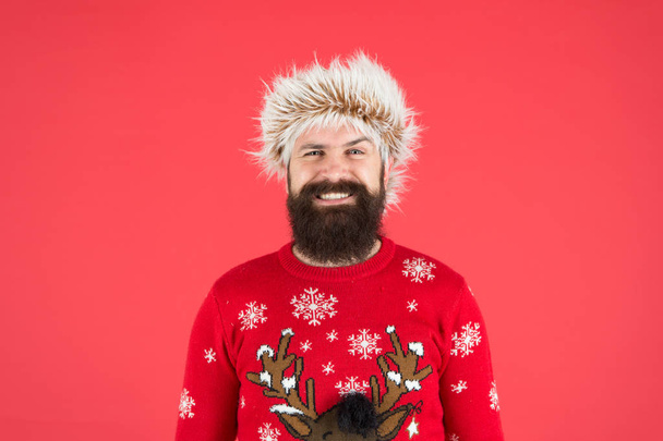 Christmas fun. happy hipster ready for xmas party. winter holiday celebration. cold weather fashion. happy new year. bearded man smiling on red background. funny man with beard in knitted sweater - Photo, image