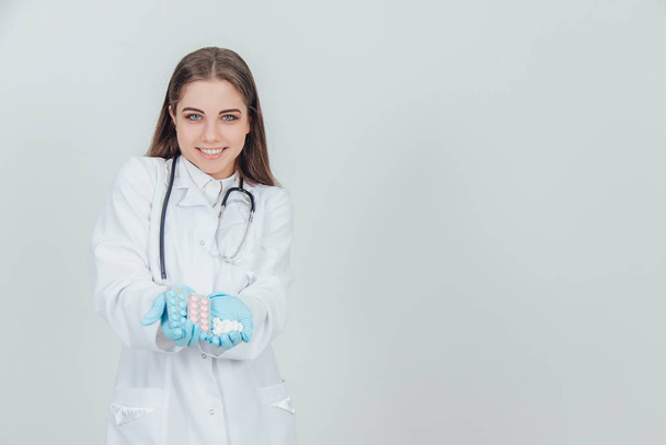 Чарівна молода медсестра стоїть з однією долонею, повною білих таблеток. Два блістерних пакетика барвистих таблеток в іншій долоні
. - Фото, зображення