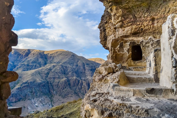 Vanis Kvabebi, klasztor jaskiń w pobliżu Wardzii w regionie Samcche - Javakheti, Gruzja, Europa. Ścieżka wzdłuż zawrotnej otchłani z widokiem na martwe góry i błękitne niebo z chmurami. - Zdjęcie, obraz