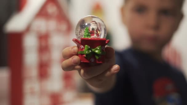 Close Up Mani Little Boy Hold Snow Globe con Babbo Natale e Calendario dell'Avvento sullo sfondo azzurrato. palla di neve di vetro - Filmati, video
