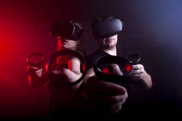 Paar in modernen Virtual-Reality-Brillen spielen einen Shooter vor dunklem Neon-Hintergrund, ein Team von Spielern in einem Spiel mit Waffen - Foto, Bild