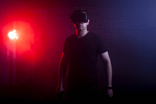 άνθρωπος με σύγχρονα γυαλιά της εικονικής πραγματικότητας κατέχει ασύρματη joysticks σε 3d φόντο, ένας τύπος είναι ένας παίκτης με gaming gadgets - Φωτογραφία, εικόνα