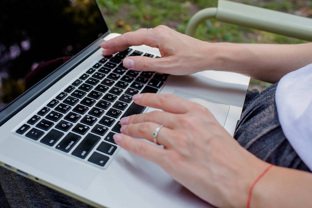 Una mujer está escribiendo en un teclado portátil. Negocios en línea al aire libre. Chica freelancer trabaja en el parque. Espacio de trabajo. Hoy en día. Trabajo remoto. Estilo de vida. Dispositivo móvil. Botones de computadora portátil de primer plano
 - Foto, imagen