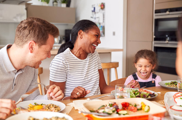 Familia de raza mixta multi-generación comiendo comida alrededor de la mesa en casa juntos
 - Foto, imagen
