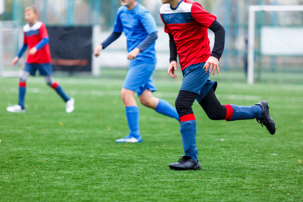Αγόρια με κόκκινα και μπλε αθλητικά παίζουν ποδόσφαιρο στο γήπεδο, ντριμπλάρουν μπάλα. Νέοι ποδοσφαιριστές με μπάλα στο πράσινο γρασίδι. Εκπαίδευση, ποδόσφαιρο, ενεργός τρόπος ζωής για τα παιδιά έννοια - Φωτογραφία, εικόνα