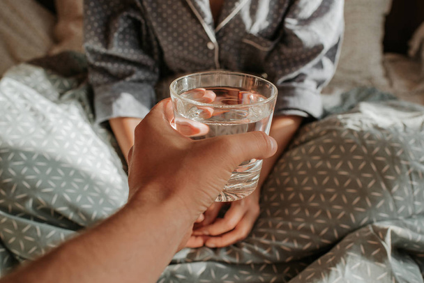 Woman in bed holding a glass of water in hand. Happy morning. Girl in pajamas. Healthy lifestyle, wellness. Proper nutrition. Drinking water. Morning with water. Sunlight on linens. Pillow, blanket - Φωτογραφία, εικόνα