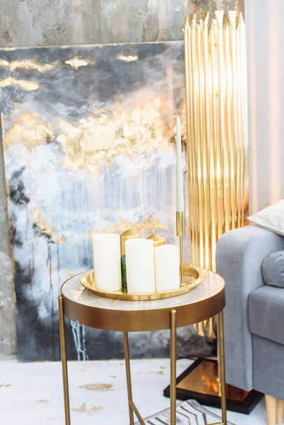 Na skleněném nočním stolku stojí tři nezapálené bílé parafinové svíčky. Drahý interiér v odstínech šedé, zlaté a modré. Zavřít - Fotografie, Obrázek