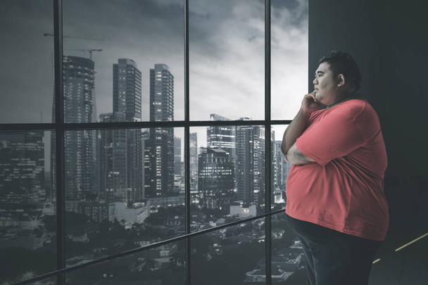 Fat Asian man staring at the cityscape pensively - Foto, Imagem