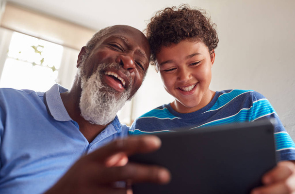 Grandfather Sitting In Chair With Grandson Watching Movie On Digital Tablet Together - Foto, imagen