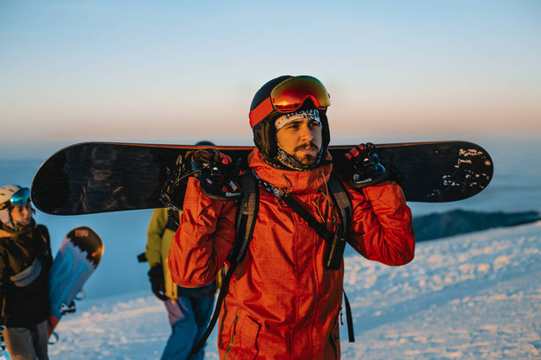 чоловік тримає сноуборд і ходить з друзями в зимових горах
  - Фото, зображення