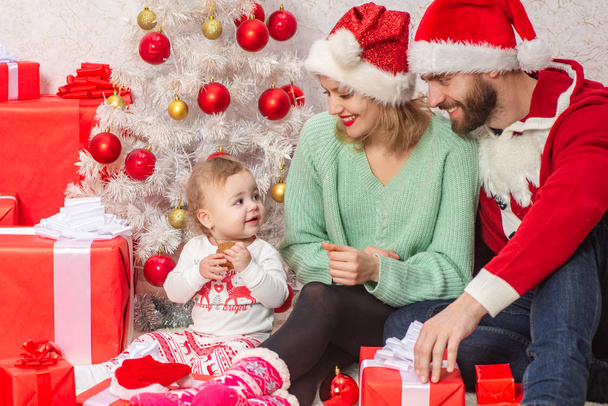 New year concept for christmas family. Baby with parents having fun near Christmas tree indoors. - Фото, изображение