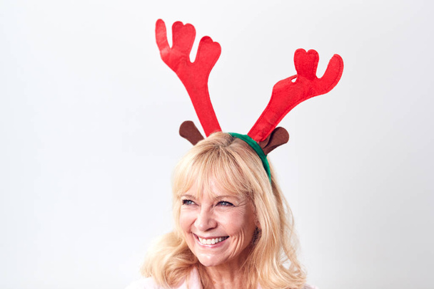 Studio Shot Of Happy Mature Woman Wearing Dressing Up Reindeer Antlers Against White Background - Фото, зображення