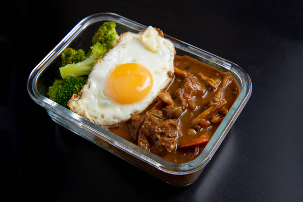Говядина карри рис в стеклянной коробке обед на черном деревянном обеденном столе
  - Фото, изображение