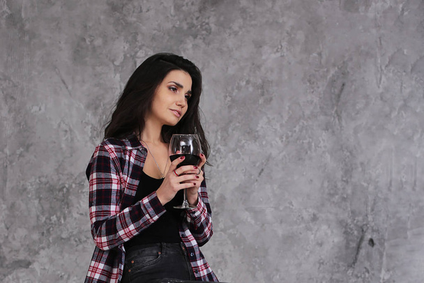 Hermosa chica delgada con pelo corto y oscuro en una camisa a cuadros de color burdeos con una copa de vino tinto en un estilo interior gris lofts
 - Foto, imagen