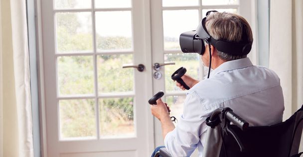 Mature Disabled Man In Wheelchair At Home Wearing Virtual Reality Headset Holding Gaming Controllers - Valokuva, kuva