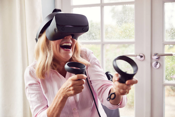 Mature Disabled Woman In Wheelchair At Home Wearing Virtual Reality Headset With Gaming Controllers - Valokuva, kuva