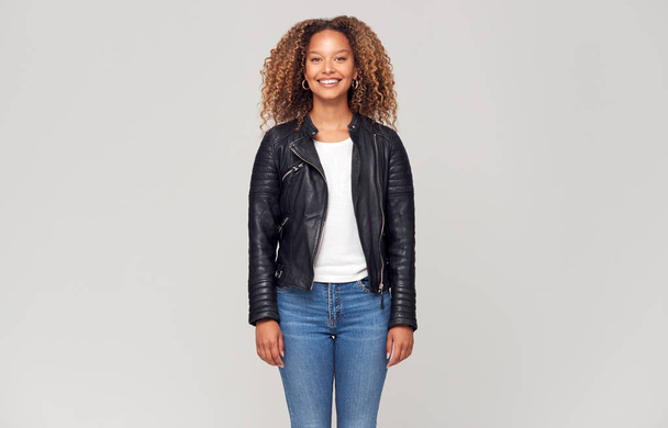 Three Quarter Length Studio Shot Of Happy Young Woman Wearing Leather Jacket Smiling At Camera - 写真・画像