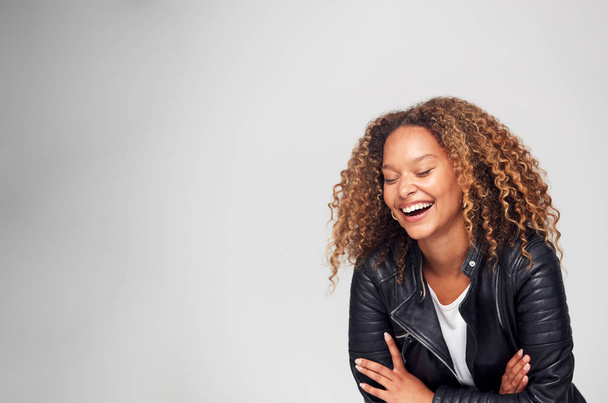 Studio Shot Of Happy Young Woman With Folded Arms Wearing Leather Jacket Laughing Off Camera - Fotografie, Obrázek