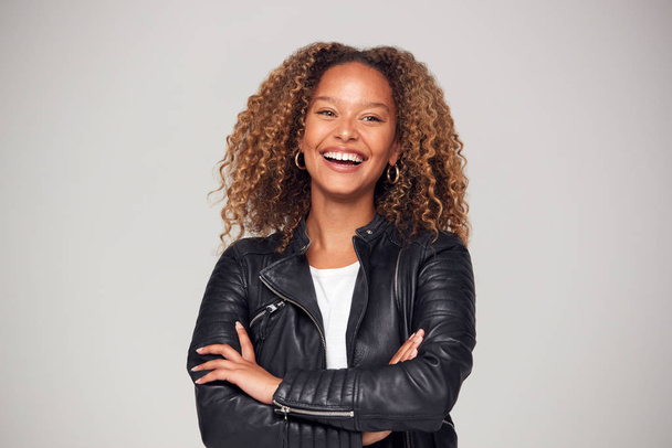 Waist Up Studio Shot Of Happy Young Woman With Folded Arms Wearing Leather Jacket Smiling At Camera - Foto, imagen