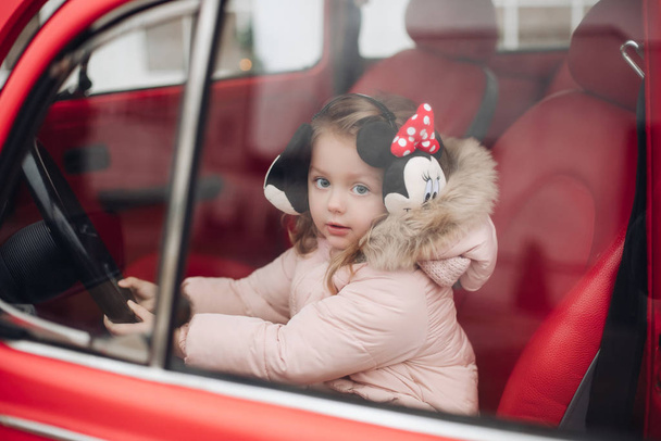 Lovely little girl in earmuffs sitting in red car. - 写真・画像