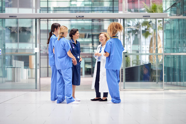 Female Medical Team Having Informal Meeting Standing In Lobby Of Modern Hospital Building - 写真・画像