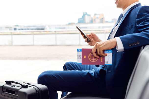 Businessman With Passport And Boarding Pass Sitting In Airport Departure Lounge Using Mobile Phone - Photo, Image