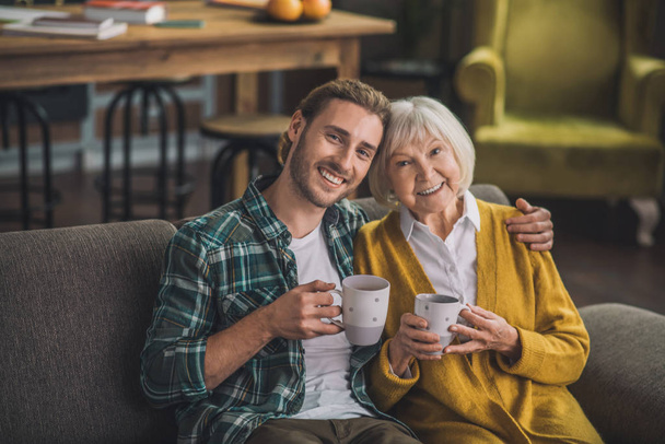 Grijsharige oudere vrouw die thee drinkt met zoon - Foto, afbeelding