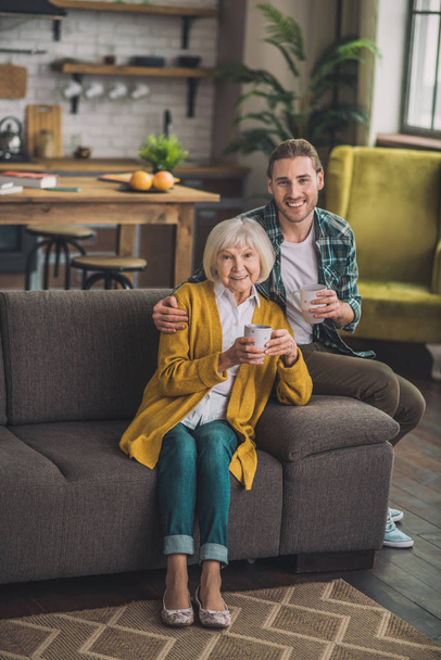 Grey-haired elderly woman sitting on the sofa with son - Foto, afbeelding