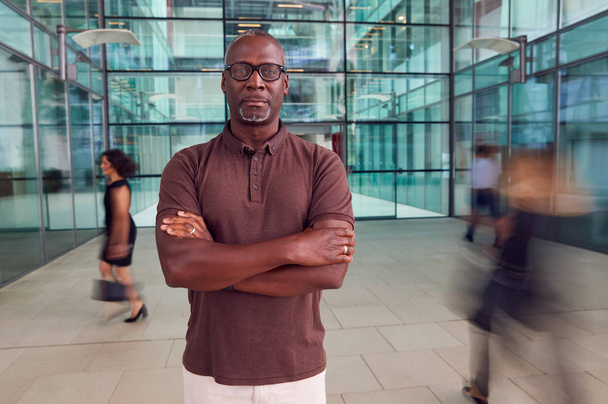 Portrait Of Mature Businessman With Crossed Arms Standing In Lobby Of Busy Modern Office - Foto, afbeelding