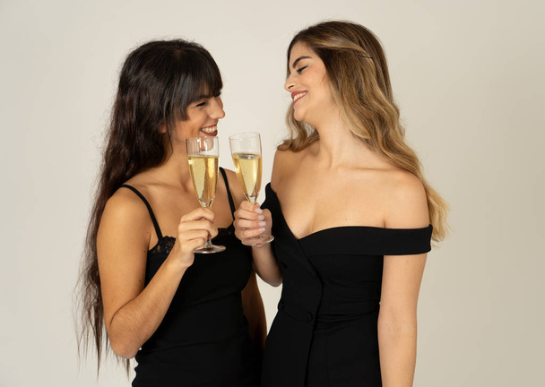 Two beautiful girlfriends having fun celebrating Christmas or New Year eve toasting glasses. Women posing in stylish sexy party dresses drinking champagne. People Friendship and Celebration. - Φωτογραφία, εικόνα