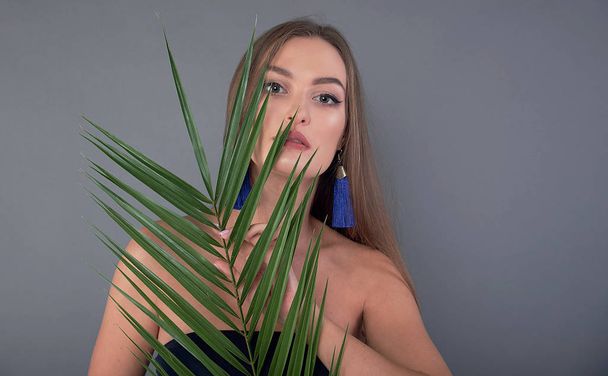 Portrait of young and beautiful woman with perfect smooth skin in tropical leaves. Concept of natural cosmetics and skincare. young beautiful woman with a palm leaf, clean skin - Photo, Image