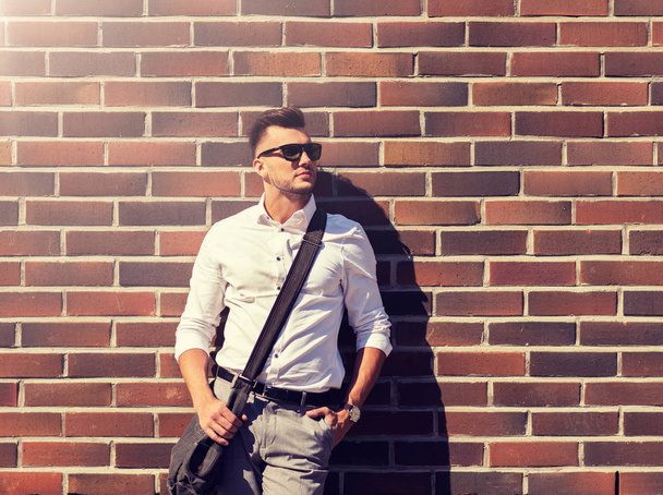 young man in sunglasses with bag over brickwall - Photo, Image