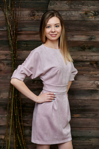 Loft style concept. Portrait of a beautiful smiling girl in a pink pretty dress on a background of interior in a room made of wood. Shows happiness, smile, kindness. Standing in front of the camera. - Фото, изображение