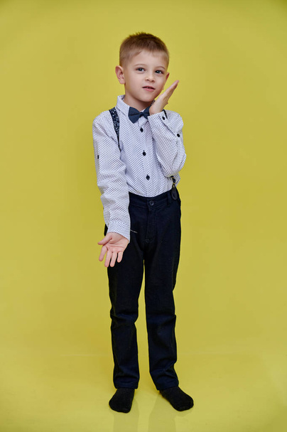 Portrait of a cute 10 years old schoolboy boy on a yellow background. Standing straight at full height, Showing emotions, talking. - Zdjęcie, obraz